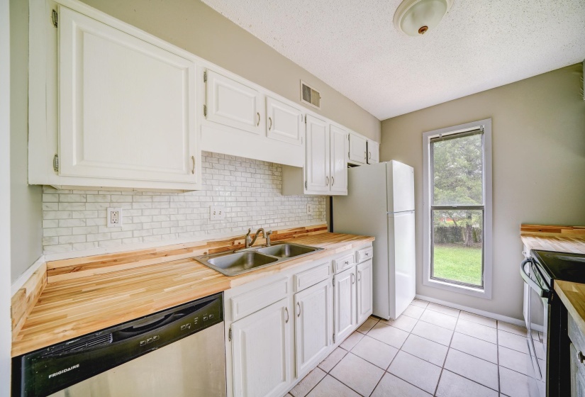 Kitchen featuring butcher block countertops, backsplash, appliances with stainless steel finishes, white cabinets, and light tile patterned floors
