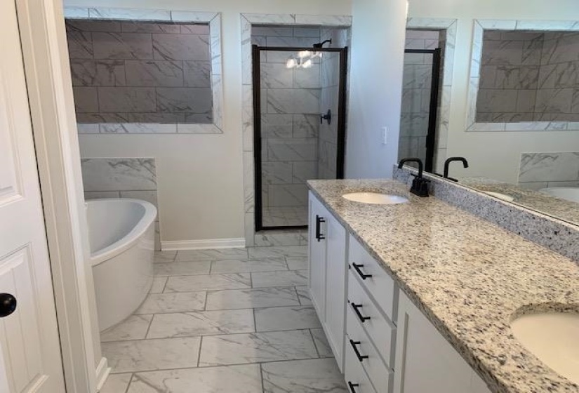 Bathroom featuring a freestanding tub, double vanity, a stall shower, marble finish floor, and a sink