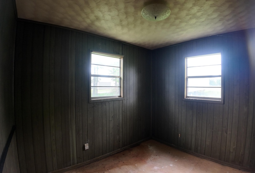 Room featuring vertical wood paneling, two windows with sills, and a flush-mount ceiling light fixture