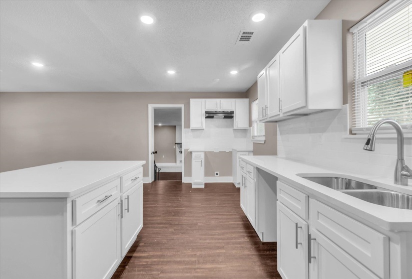 Kitchen featuring a large island, white cabinetry, undermount double-basin sink with a gooseneck faucet, light countertops, and wood-finish flooring