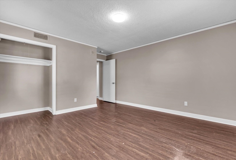 Room featuring wood-finish flooring, neutral wall paint, white baseboards, and white crown molding