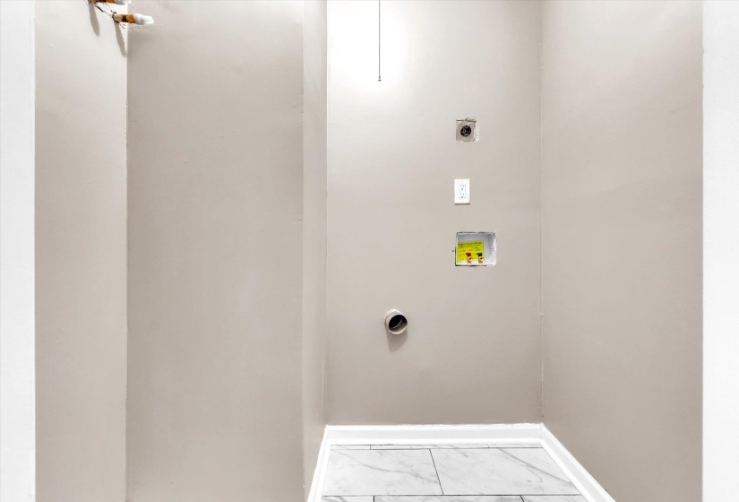 Utility area featuring light beige walls, white baseboards, and grey tile flooring