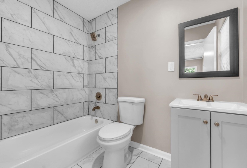 Contemporary bathroom featuring a white tub with subway-style wall tile, a neutral-toned vanity with a white basin sink, a framed mirror, and coordinating floor tiles