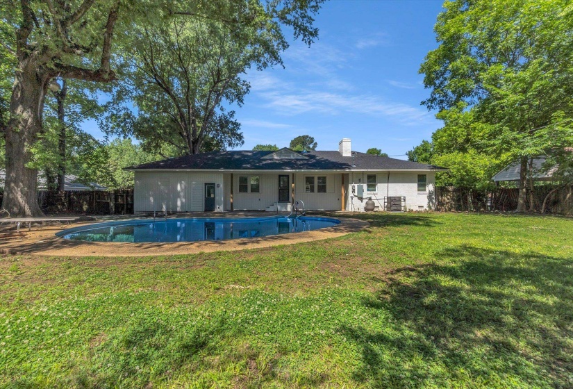 Spacious backyard featuring an in-ground swimming pool, expansive lawn, mature shade trees, and a white exterior home with a dark roof