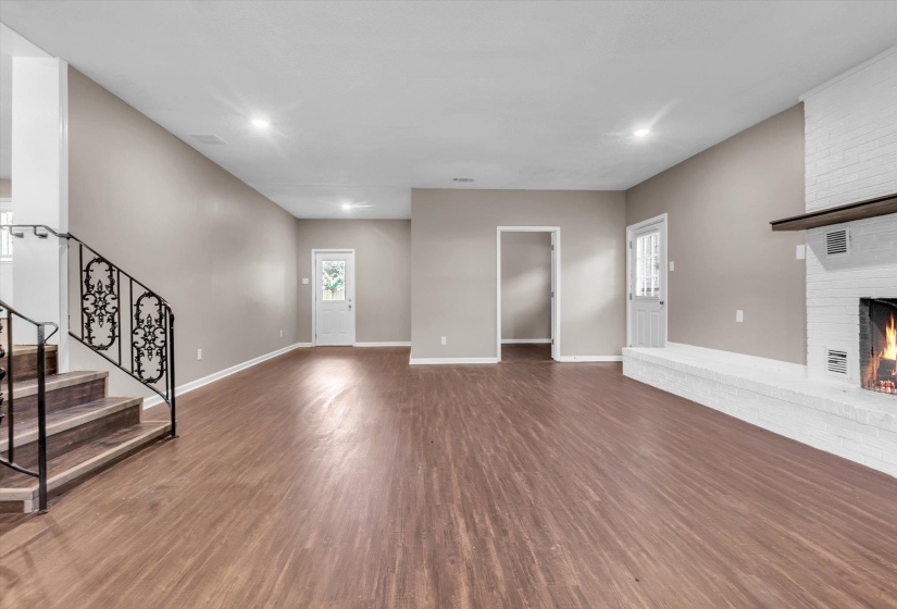 Spacious interior featuring wood-finish flooring, a white painted brick fireplace with a dark wood mantel, and a staircase with decorative wrought iron railings