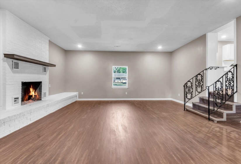 Spacious interior featuring wood-finish flooring, a white brick fireplace with a wood mantel, and a decorative wrought iron staircase