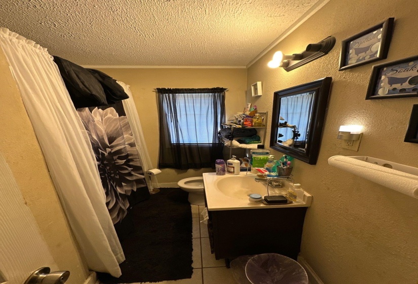 Bathroom featuring a single vanity with a laminate countertop, a standard toilet, and a window with blinds