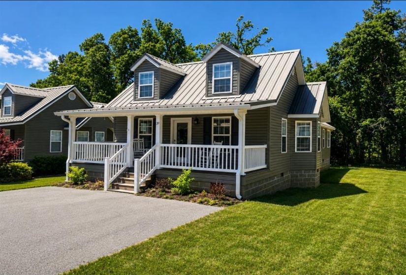 Charming cottage-style home featuring a gray exterior, white porch railings, a metal roof, dormer windows, and a paved driveway!