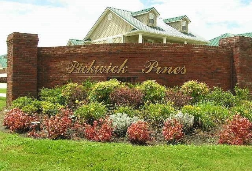 Brick entrance monument with gold-toned lettering, featuring a varied landscape bed with established plantings
