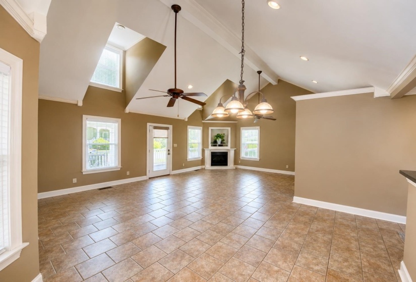 Vaulted ceiling with exposed beams, tile flooring, recessed lighting, ceiling fan, and a corner fireplace with mantel