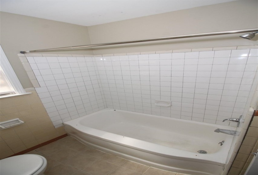 Bathtub with white subway tile surround, chrome shower rod, and chrome faucet fixtures