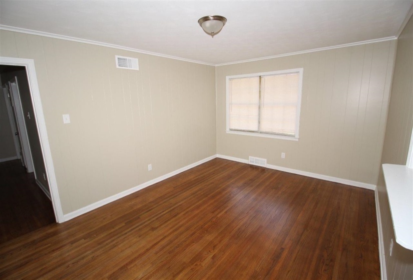 Spacious room featuring wood-finish flooring, light-toned walls with vertical paneling, and a white window frame with blinds