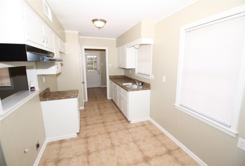 Functional kitchen featuring white cabinetry, laminate countertops, a double basin sink, tile flooring, and a ceiling-mounted light fixture