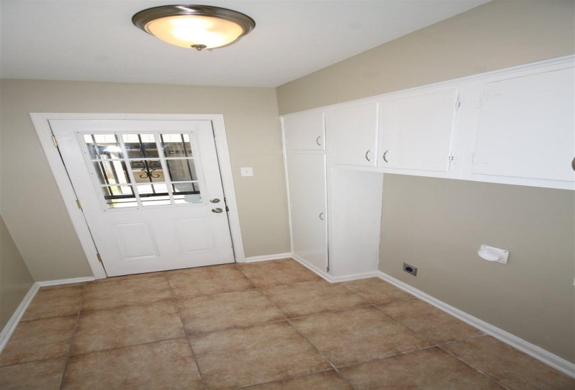 Utility room featuring extensive white cabinetry, durable tile flooring, a glass-paned exterior door, and a flush-mount ceiling light fixture