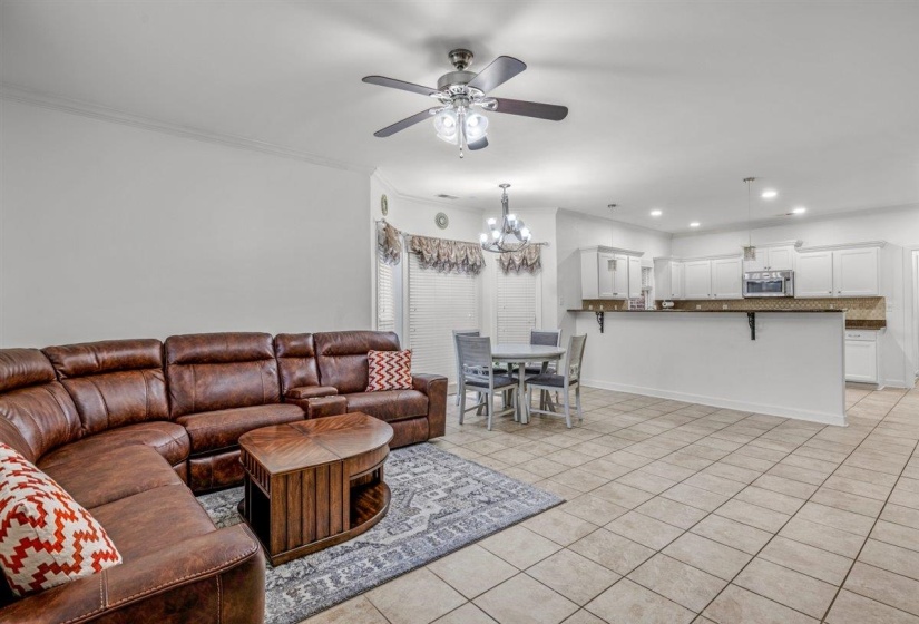 Open-concept living area featuring tile flooring, white walls, and crown molding