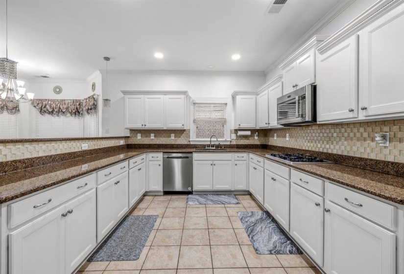 U-shaped kitchen with white cabinetry, stainless steel appliances, dark stone countertops, and tile backsplash