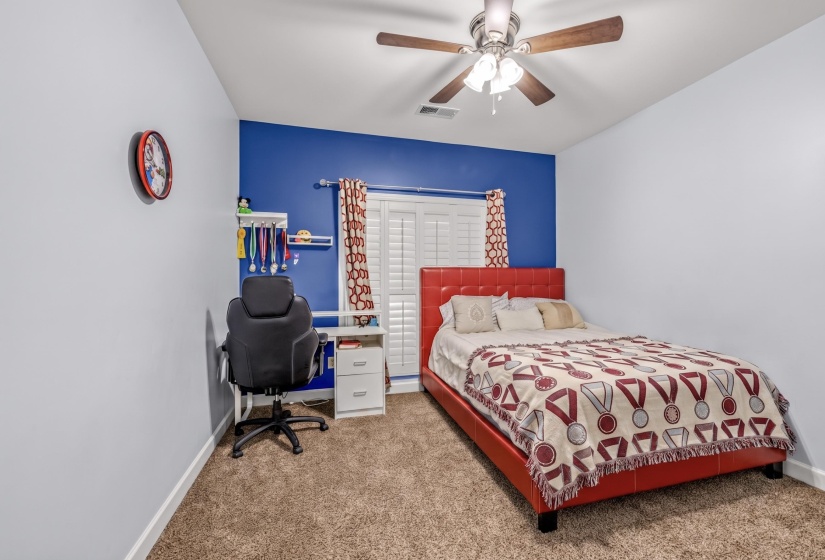 Carpeted interior room featuring a contrasting accent wall, ceiling fan with light fixture, and white louvered window shutters