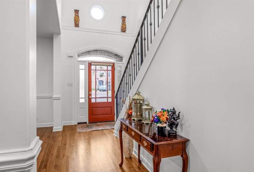 Entry foyer featuring wood-finish flooring, a red front door with sidelights, an arched transom, and a high ceiling with a circular window