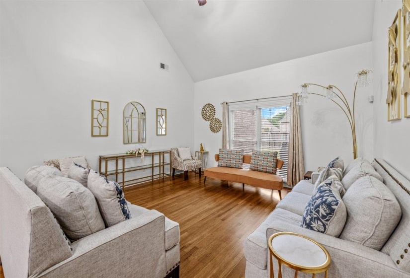 Spacious living area featuring high vaulted ceilings, wood-finish flooring, and a large window with privacy blinds