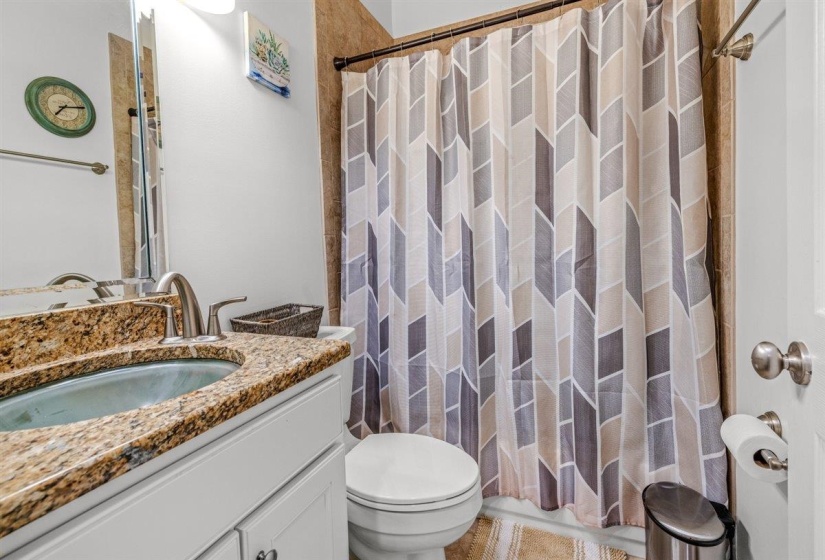 Bathroom featuring a granite-look countertop with an undermount sink, white vanity cabinetry, a tiled shower surround, and a coordinating floor tile