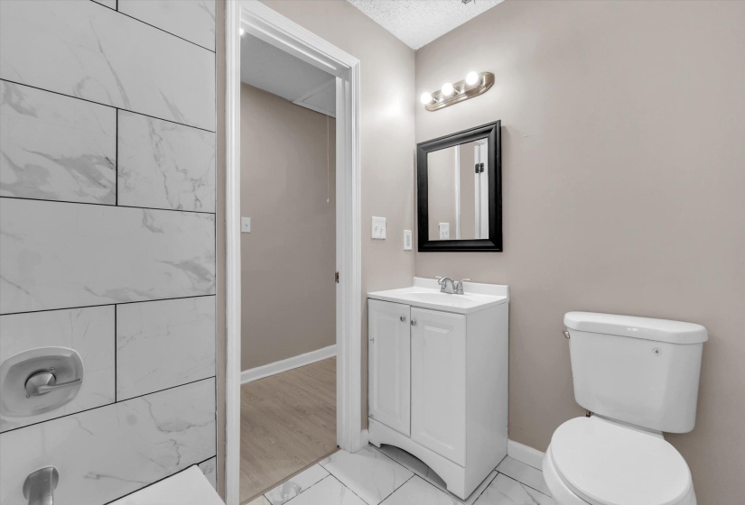 Bathroom featuring large format white tile flooring and shower surround, a white vanity with integrated sink, a dark framed mirror, and a three-light vanity fixture