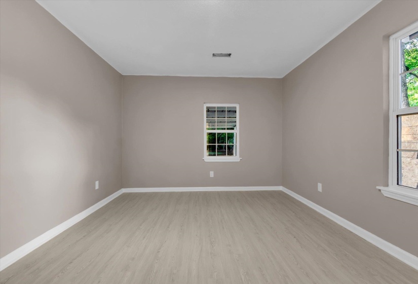 Spacious room featuring light wood-finish flooring, neutral wall paint, white baseboards, and multiple windows