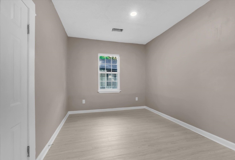 Bright room featuring neutral wall paint, light wood-finish flooring, white baseboards, and a single window with white trim