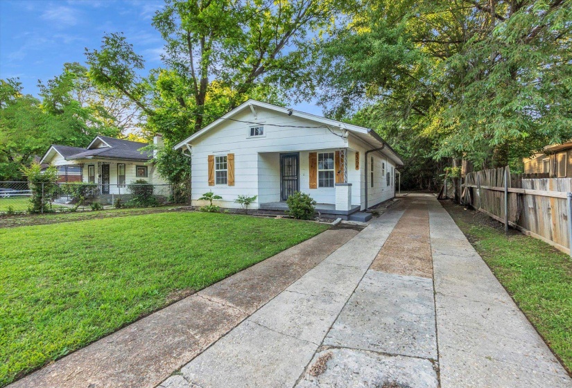 White siding exterior with a covered front porch, wood window shutters, a front lawn, a concrete driveway, and a wood privacy fence