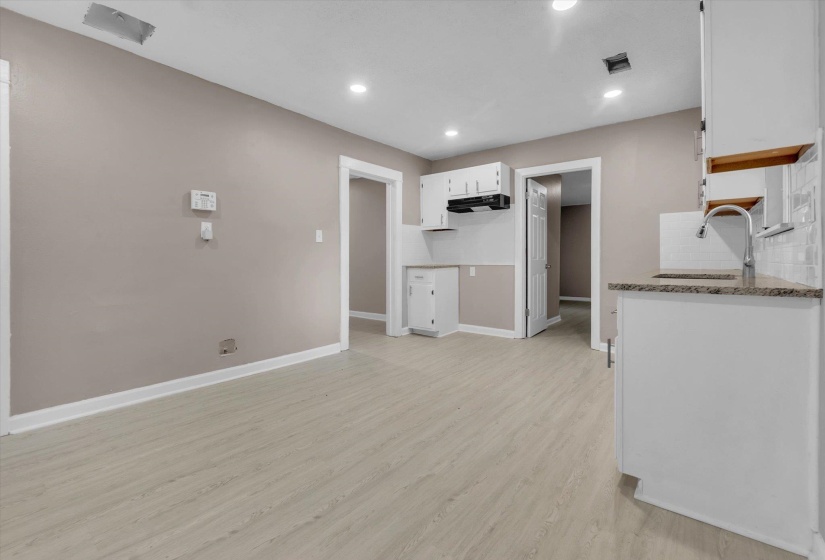 Open-concept kitchen and living area featuring light wood-finish flooring, recessed ceiling lighting, granite countertops, a subway tile backsplash, and white cabinetry