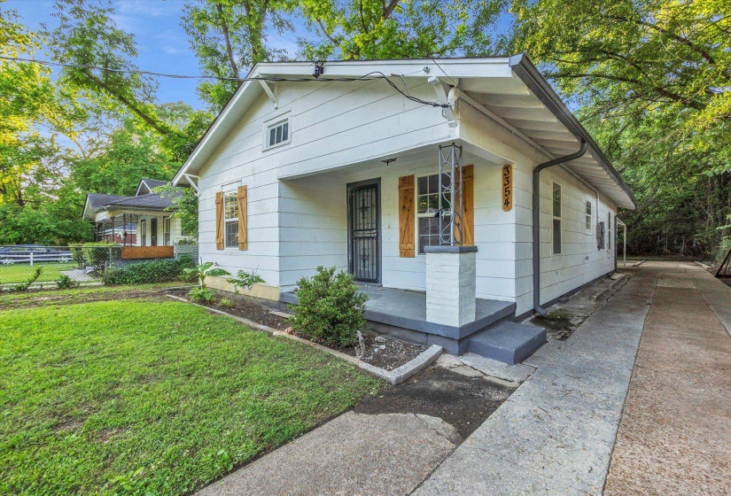 White siding exterior with wood shutters, a covered front porch, and a concrete driveway