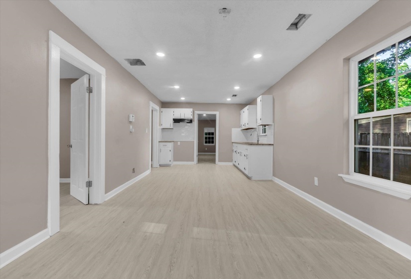 Spacious open-concept room featuring light-toned wood-finish flooring, recessed lighting, neutral wall paint, and white trim