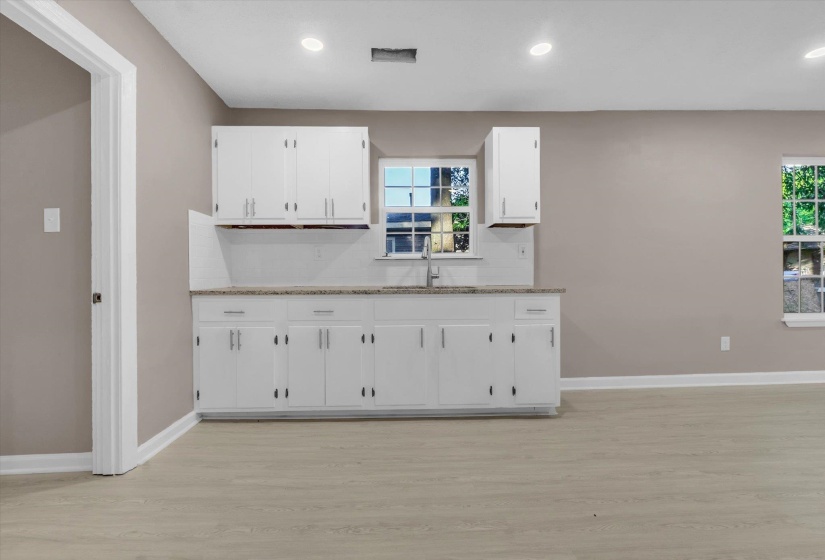 Kitchenette featuring white cabinetry, light-toned countertops, a stainless steel sink, and wood-finish flooring
