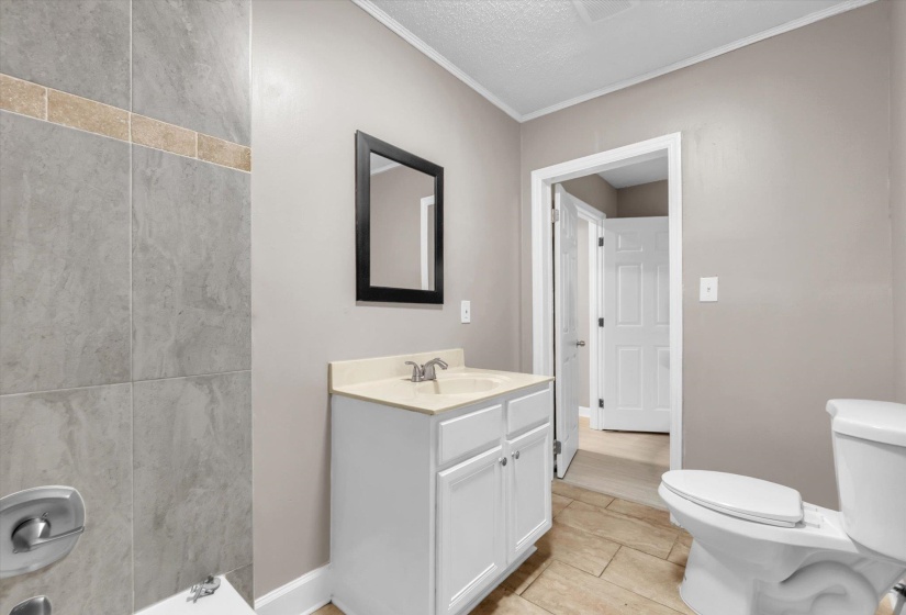Bathroom featuring a white vanity with a light-toned countertop, a framed mirror, a toilet, and a tiled shower surround with an accent band
