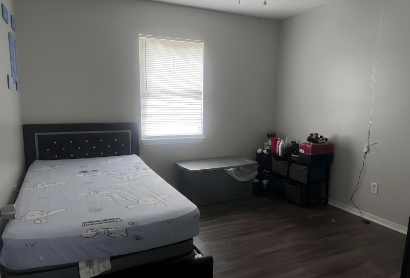 Room featuring wood-finish flooring, a bright window with blinds, and light-toned walls