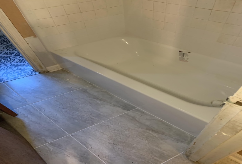 White bathtub with coordinating white subway tile surround and gray rectangular floor tiles