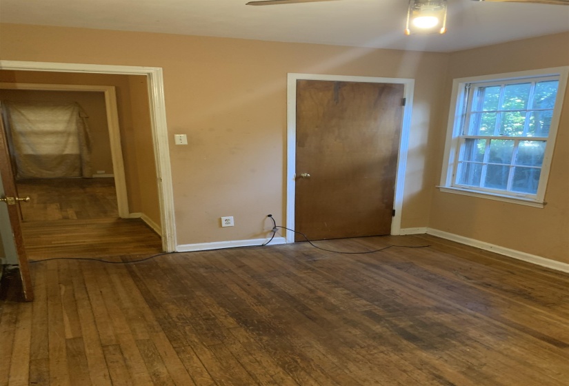Hardwood flooring extends throughout this room, featuring a double-hung window with natural light, a ceiling-mounted light fixture, and a solid wood door