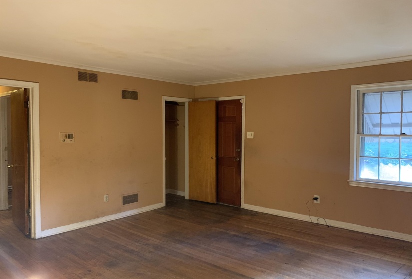 Spacious room featuring wood-finish flooring, a window with exterior visibility, crown molding, and two interior doorways