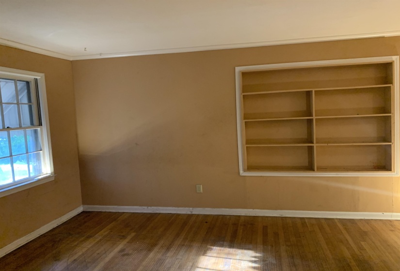 Interior space featuring wood-finish flooring, built-in shelving, a double-hung window, crown molding, and baseboards