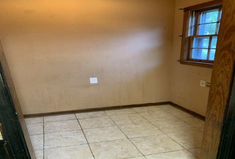 Compact room featuring a multi-pane window with wood trim, light-toned ceramic tile flooring, and a baseboard molding