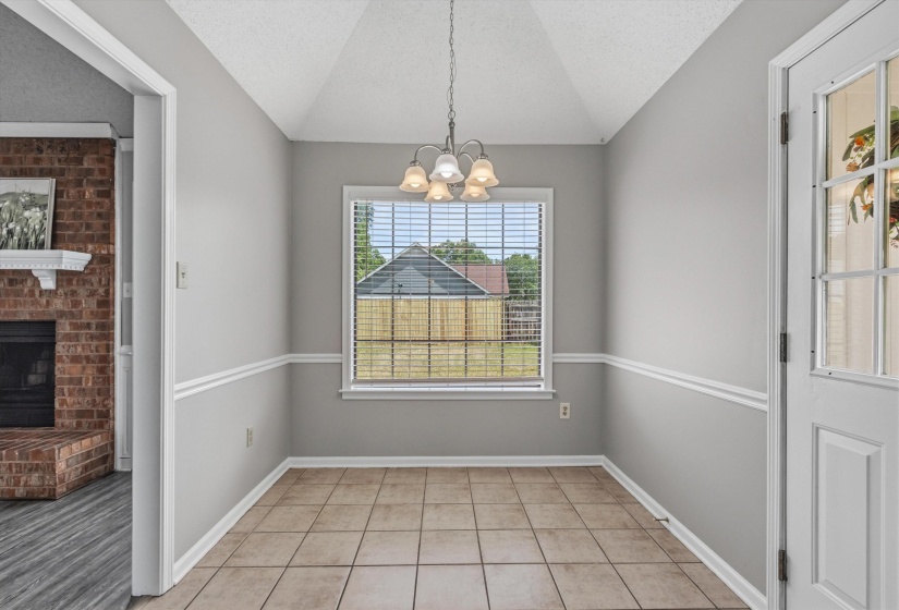 Dining area featuring a vaulted ceiling with a chandelier, tile flooring, window with blinds, and decorative chair rail molding
