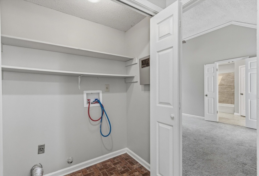 Dedicated laundry space featuring two built-in shelves, brick-patterned flooring, and a utility panel