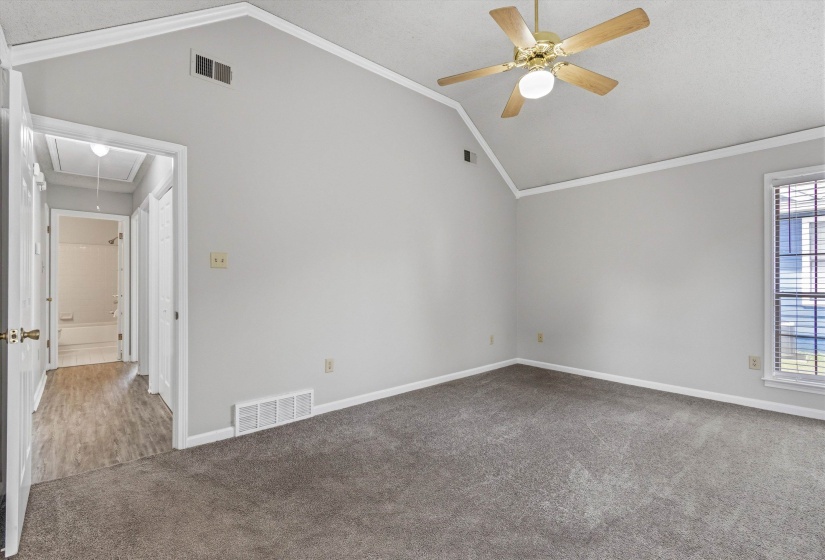 Spacious room featuring vaulted ceilings, a ceiling fan with integrated lighting, wall-to-wall carpeting, and a window with blinds