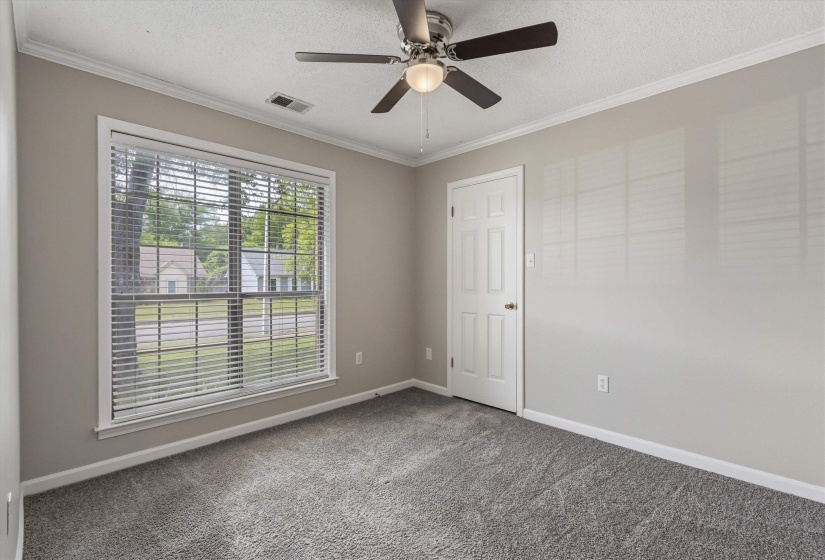 Carpeted interior space featuring a large window with blinds, ceiling fan with light fixture, neutral wall paint, white trim, and a white six-panel door