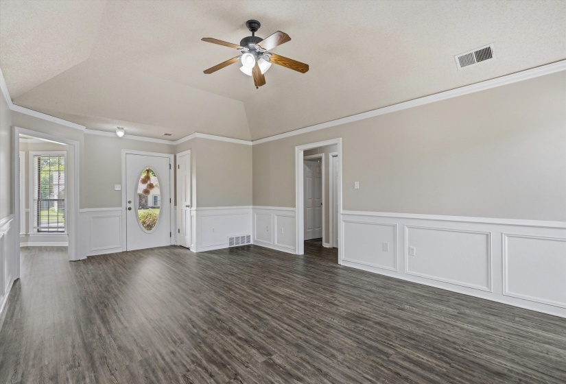 Spacious interior featuring wood-finish flooring, wainscoting, a vaulted ceiling, and a ceiling fan with integrated lighting