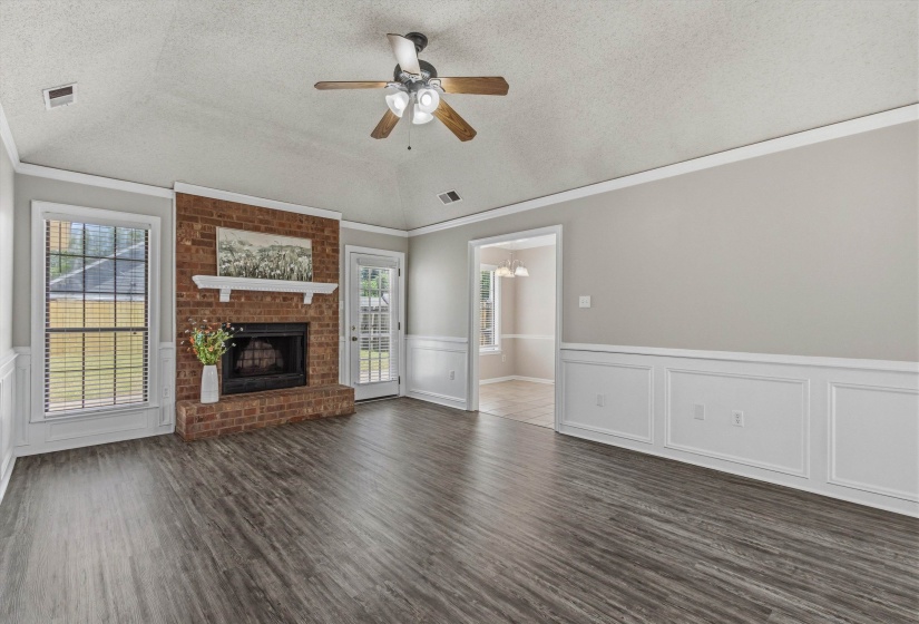 Spacious living area featuring a brick fireplace with a white mantel, wood-finish flooring, and white wainscoting