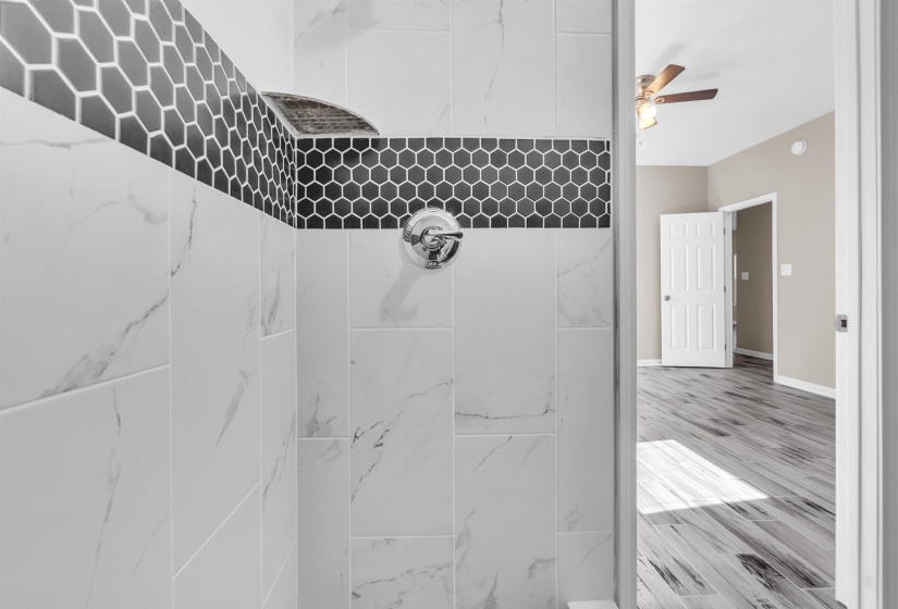 Shower interior featuring large-format white tile with subtle veining, dark gray hexagonal mosaic accent tile, and a built-in corner shelf