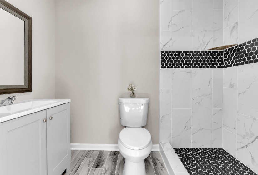 Shower featuring white marble-look tile with a black hexagon tile accent band and floor
