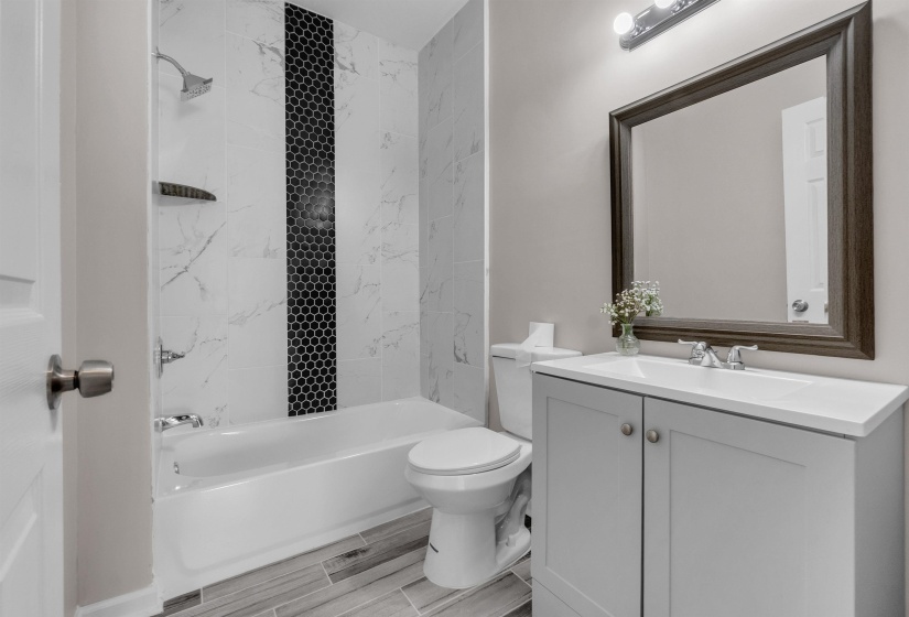 Bathroom featuring a shower/tub combination with white marble-look tile, a black hexagon tile accent strip, and a wood-finish flooring