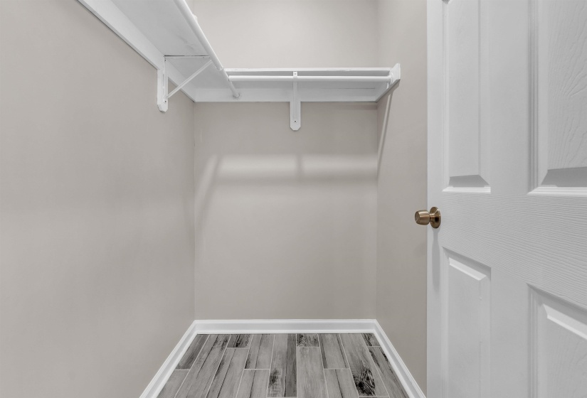 Storage closet featuring white-painted shelving and hanging rod system, light gray wall paint, and wood-look tile flooring