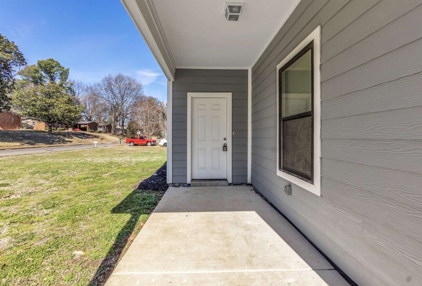 Covered concrete porch with light gray siding exterior and white trim around the window and door
